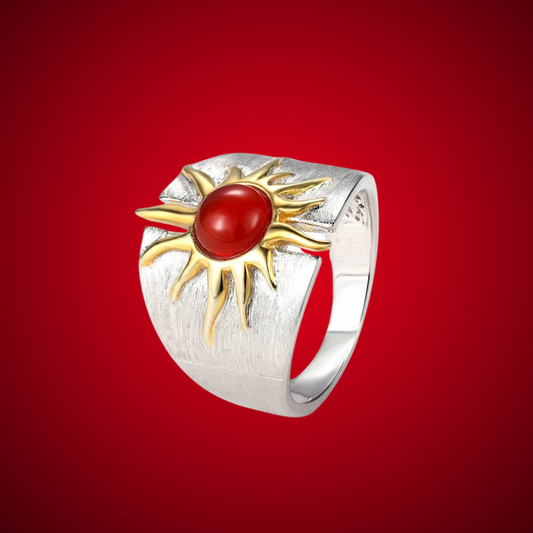 Wide silver ring with a central red cabochon framed by gold sun-ray detailing.

