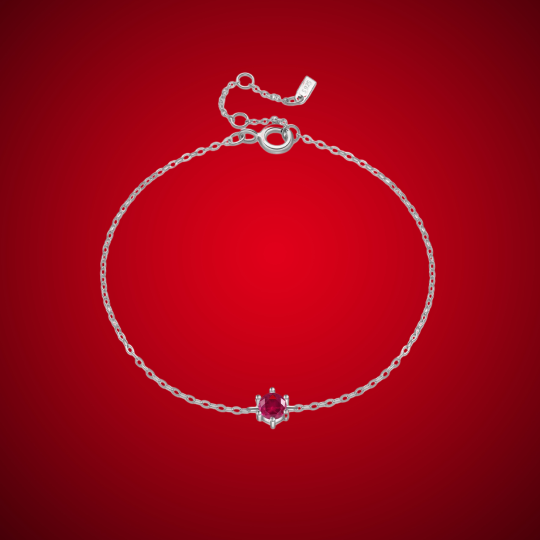 Delicate silver bracelet featuring a single round red stone set at the center.

