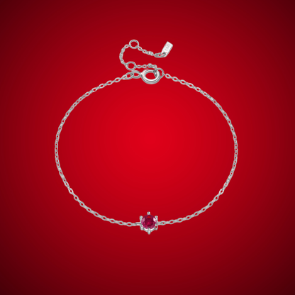 Delicate silver bracelet featuring a single round red stone set at the center.

