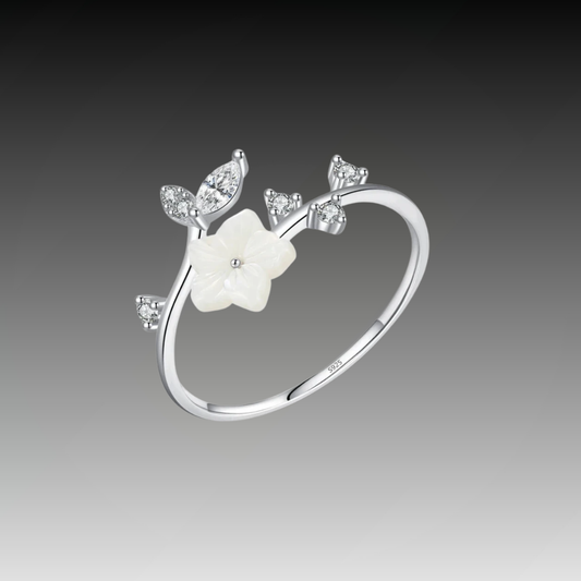 Delicate silver ring featuring a white carved flower and sparkling leaf-shaped stones arranged in a graceful, curved design.

