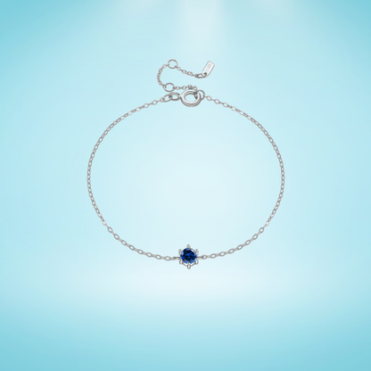 Delicate silver chain bracelet with a single round deep blue gemstone in a minimalist prong setting