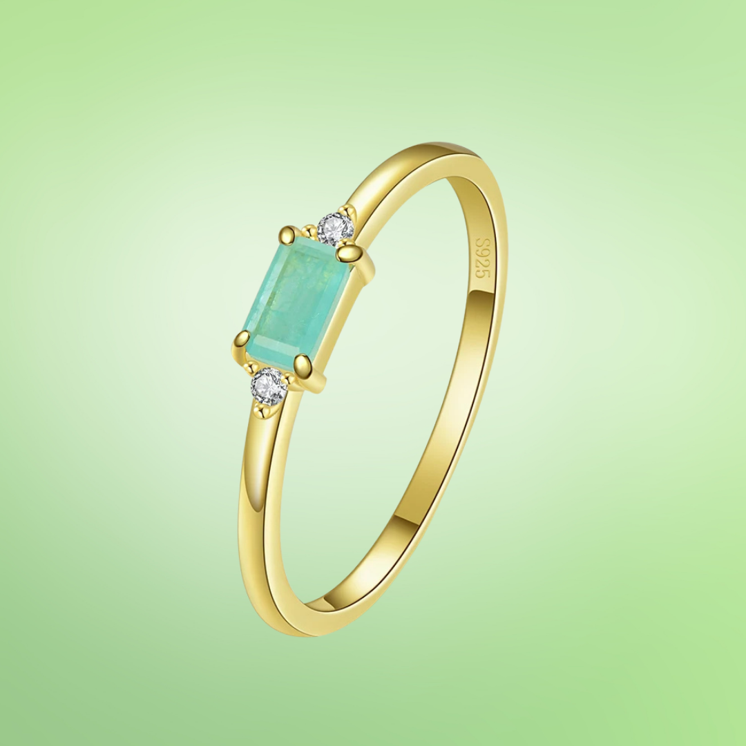 Delicate gold ring with a rectangular light green stone and two small clear side stones.

