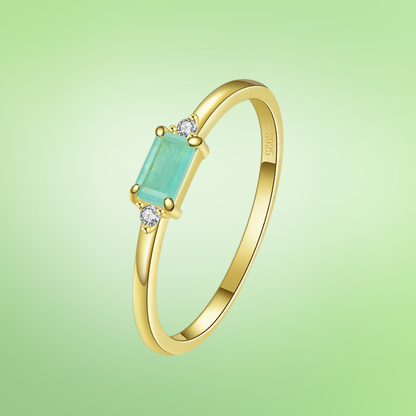 Delicate gold ring with a rectangular light green stone and two small clear side stones.

