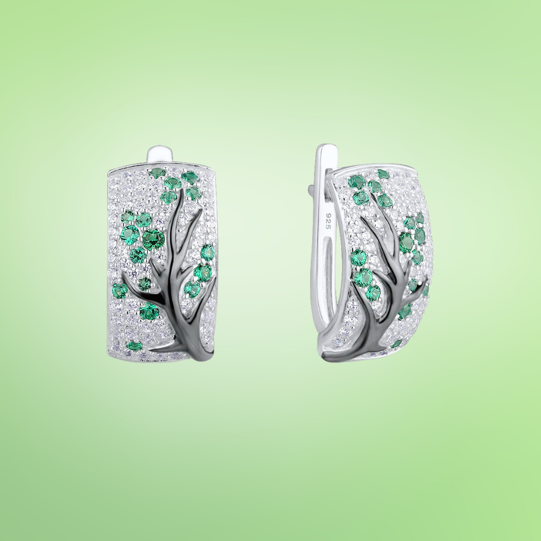 Silver earrings with raised black tree branches and scattered green and white stones

