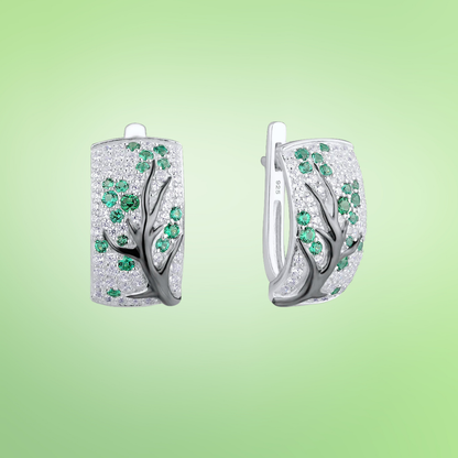 Silver earrings with raised black tree branches and scattered green and white stones

