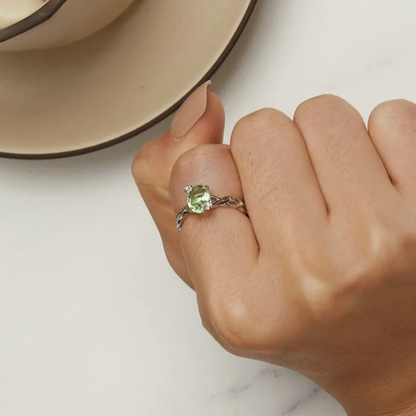 Silver ring with green round gemstone and vine-inspired band design

