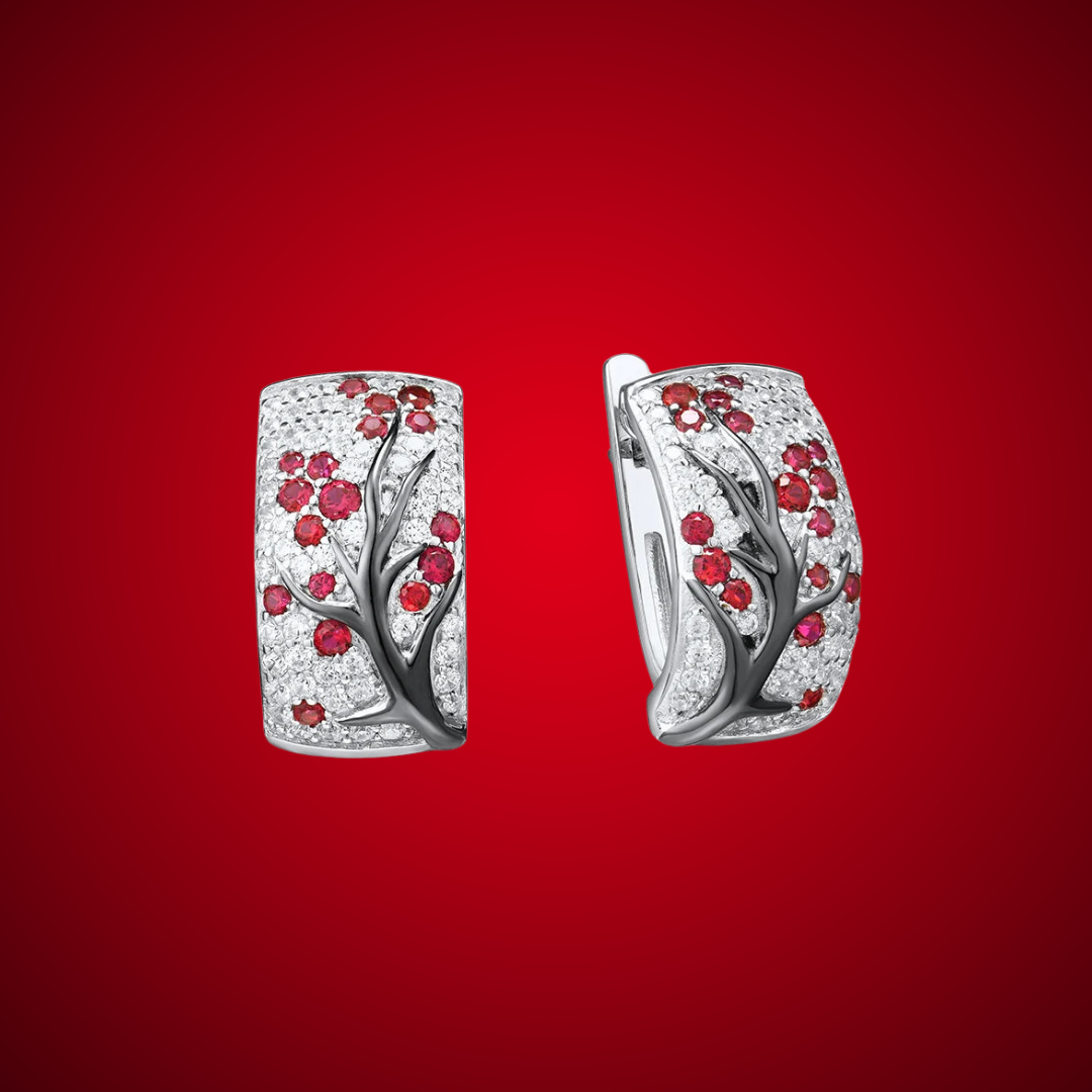 Silver earrings featuring raised black branches with scattered red blossom-like stones.

