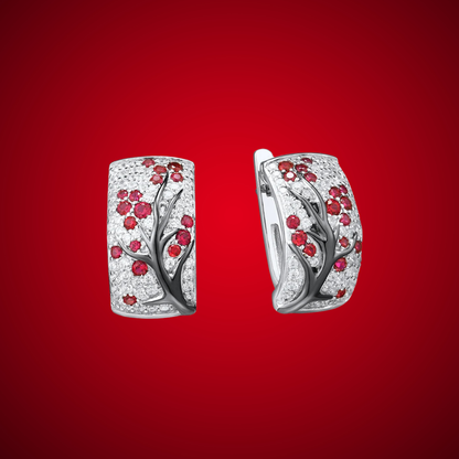 Silver earrings featuring raised black branches with scattered red blossom-like stones.

