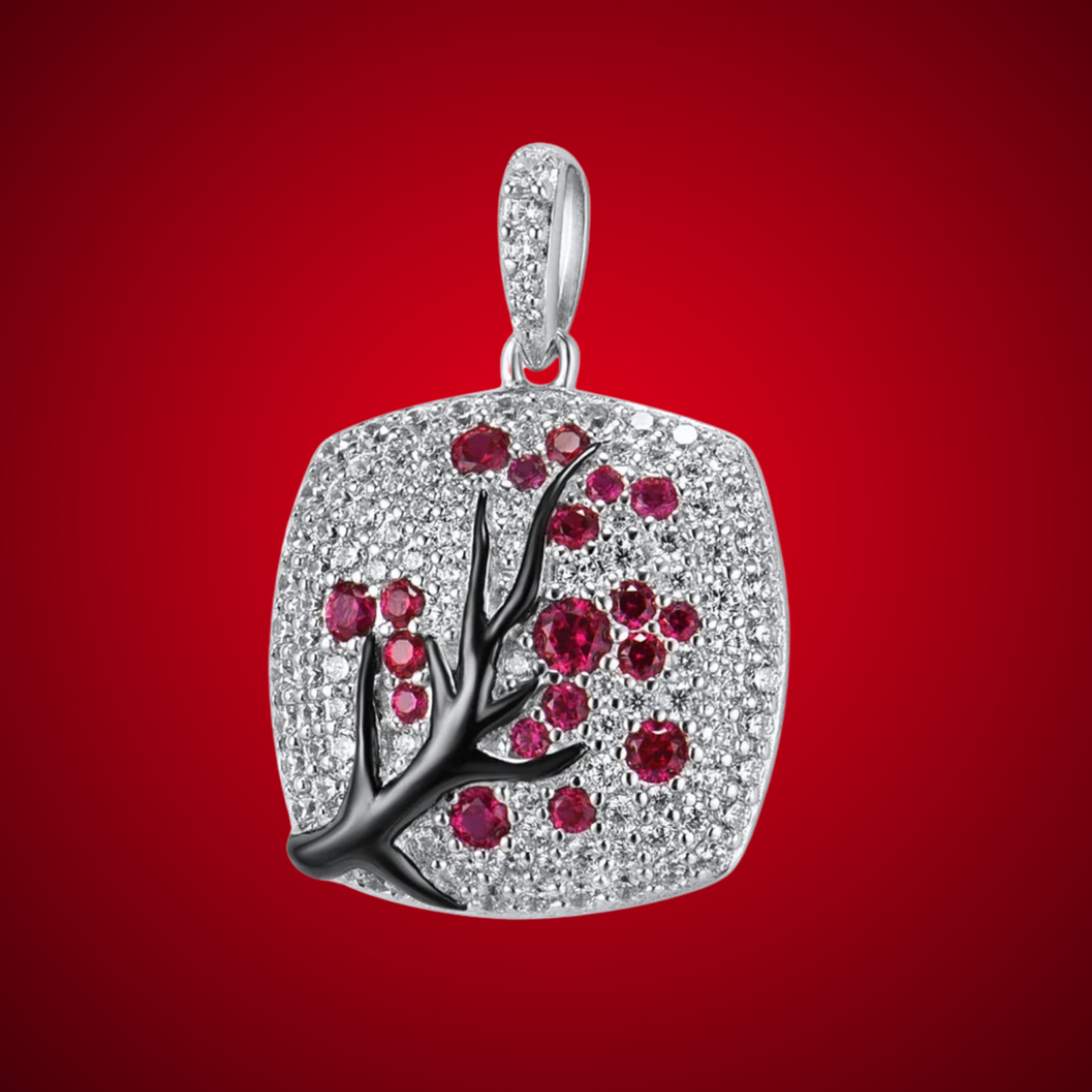 Square silver pendant featuring a black branch with red stones arranged like blossoms.

