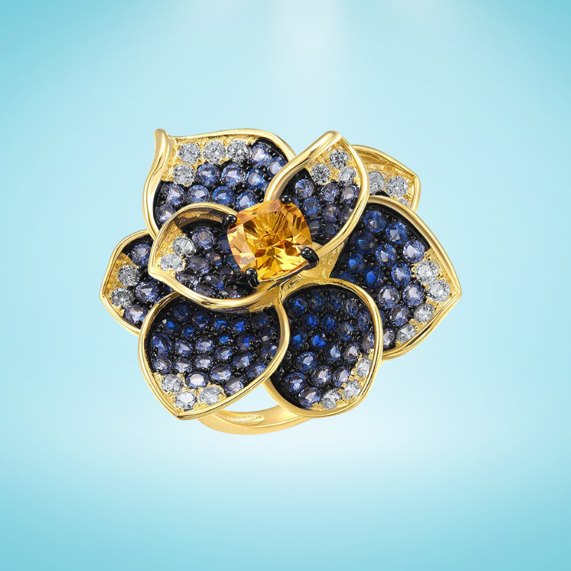 Statement floral ring in gold plating, with deep blue and clear pavé stones and a golden-yellow center gem

