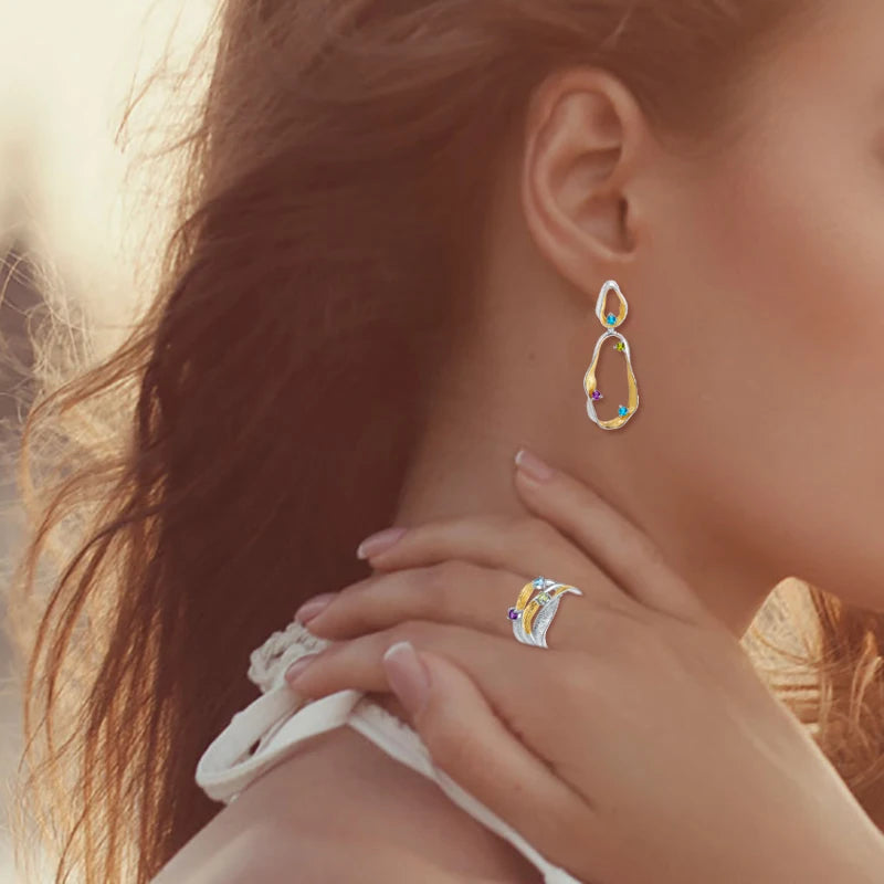 Dangling earrings with flowing gold and silver forms set with turquoise-colored stones

