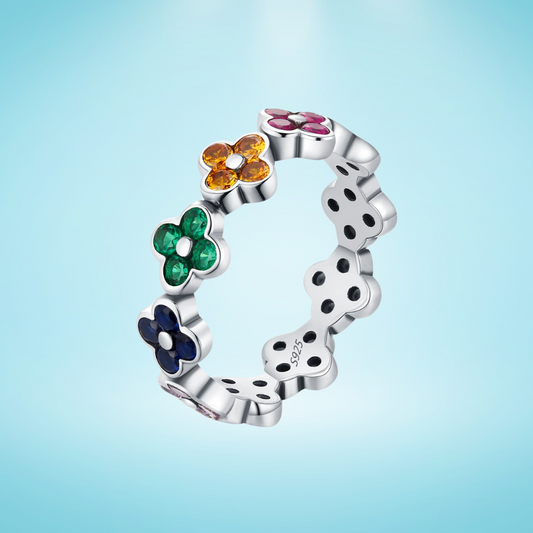 Silver ring with multicoloured four-petal flower gemstones set around the band.

