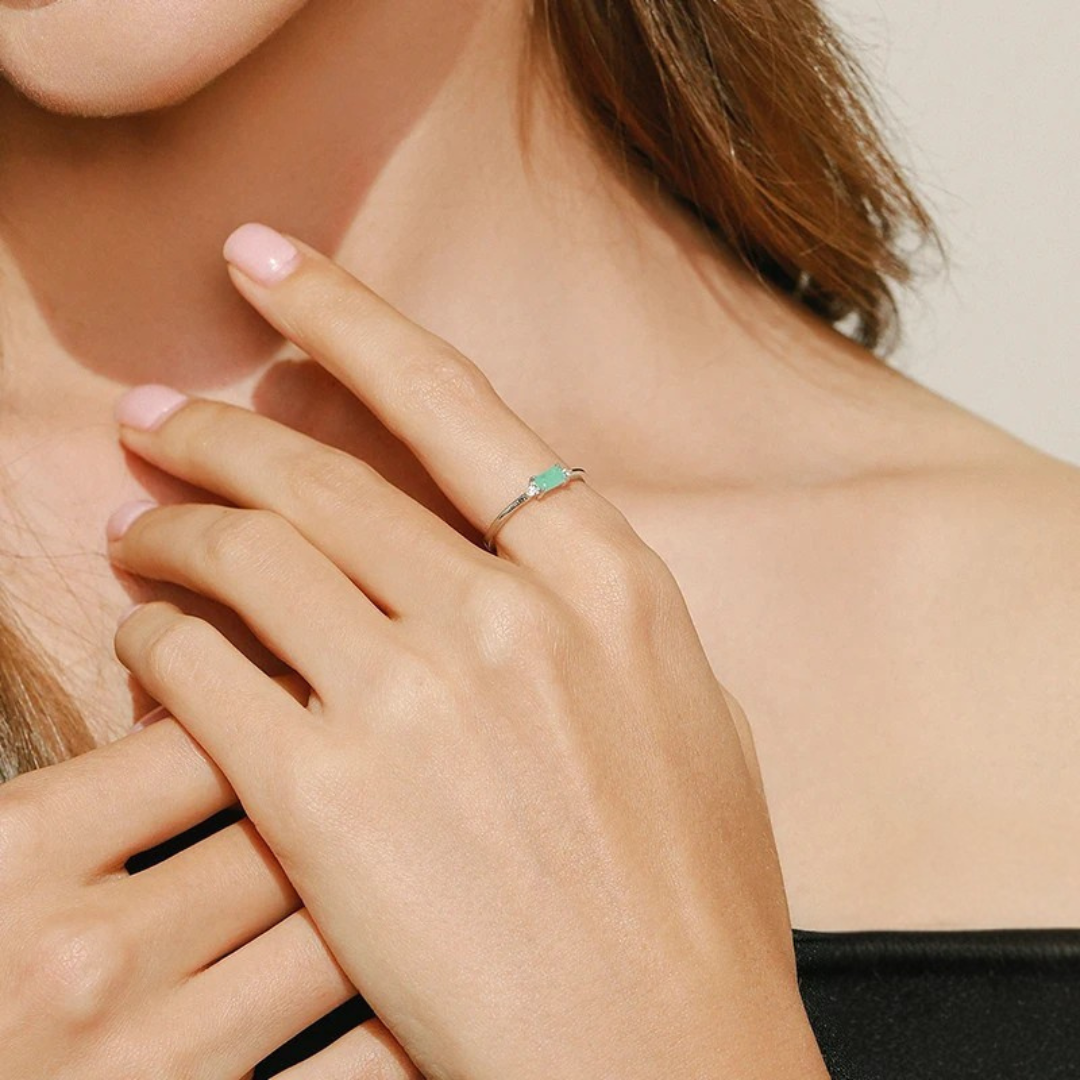 Delicate gold ring with a rectangular light green stone and two small clear side stones.

