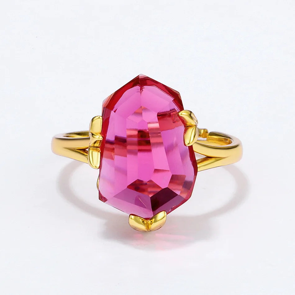 Gold ring with a bold, faceted pink gemstone held by petal-shaped prongs, displayed on a red background.

