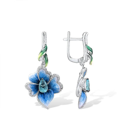 Silver floral earrings with hand-painted blue petals, green enamel accents, and teardrop blue stones.

