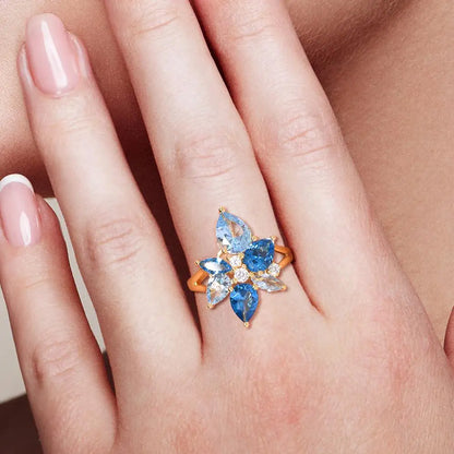 Gold-plated ring with a cluster of blue and clear gemstones in marquise and pear cuts arranged like flower petals

