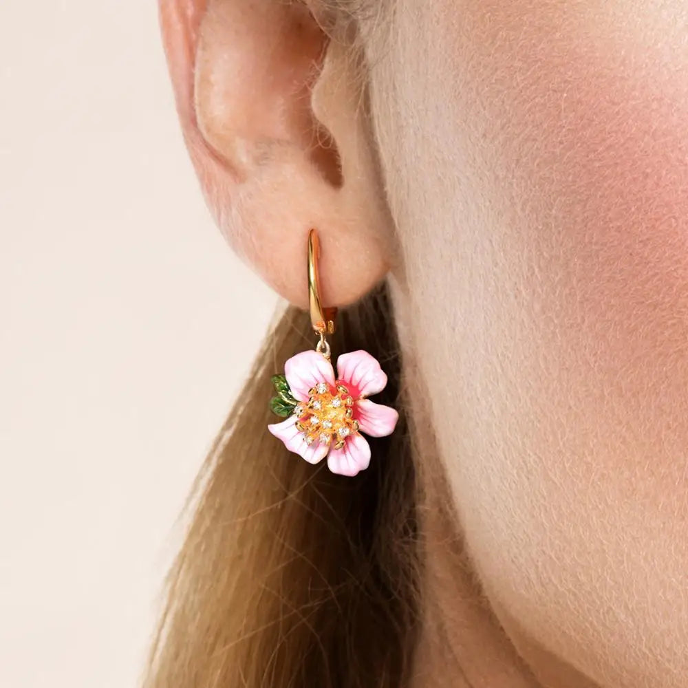Prato earrings featuring soft pink flower petals, golden centers with crystal accents, and green enamel leaves.

