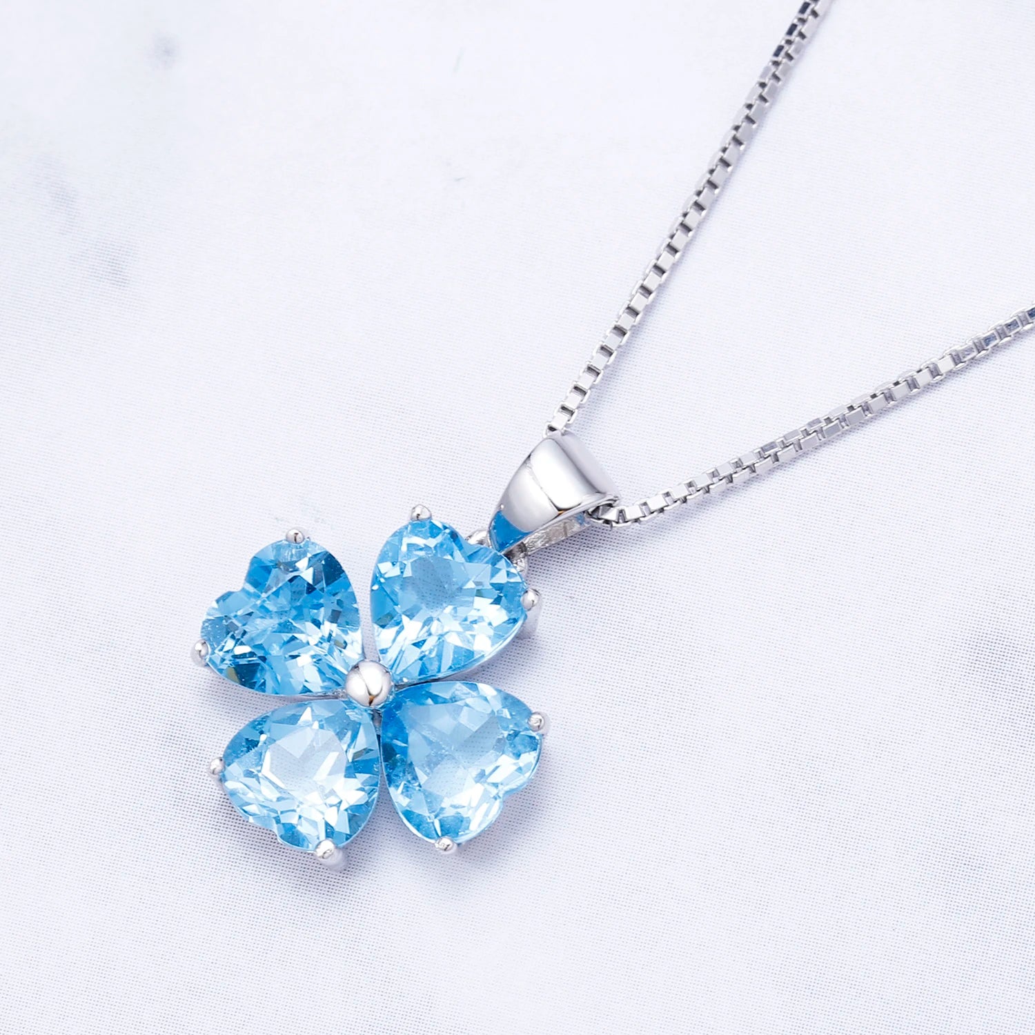 Silver pendant featuring four heart-cut light blue stones arranged in a floral shape

