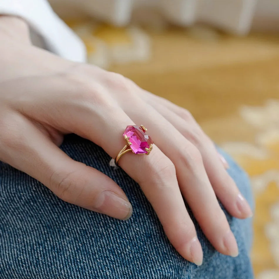 Gold ring with a bold, faceted pink gemstone held by petal-shaped prongs, displayed on a red background.

