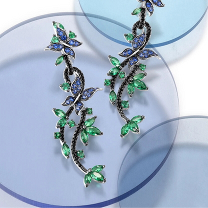 Long silver earrings with blue and green crystal butterflies and vine-like detailing

