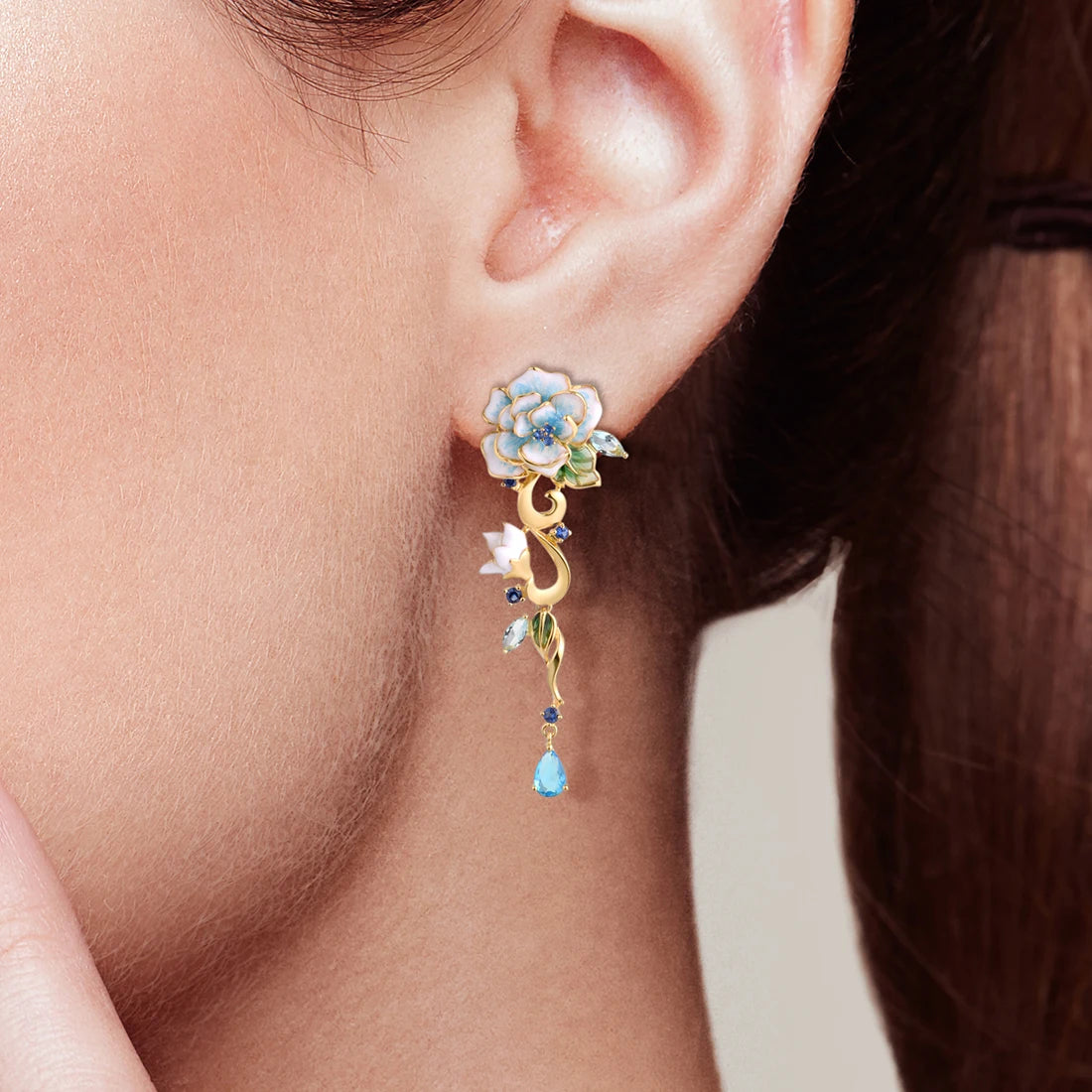 Gold floral earrings with hand-painted white and blue enamel petals, sapphire accents, and dangling blue teardrop stones

