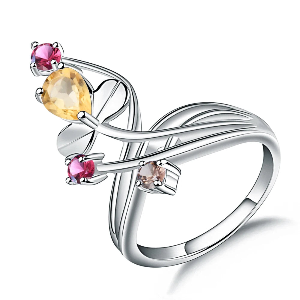 Silver ring with a flowing, branch-like design, featuring a pear-shaped yellow gemstone and smaller pink and light brown stones.

