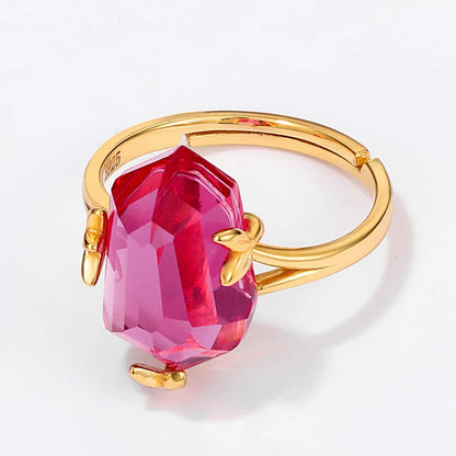 Gold ring with a bold, faceted pink gemstone held by petal-shaped prongs, displayed on a red background.

