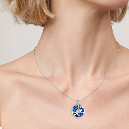 Sterling silver circular pendant with floral blue enamel designs and a central open circle, featuring stylized flowers and leaves