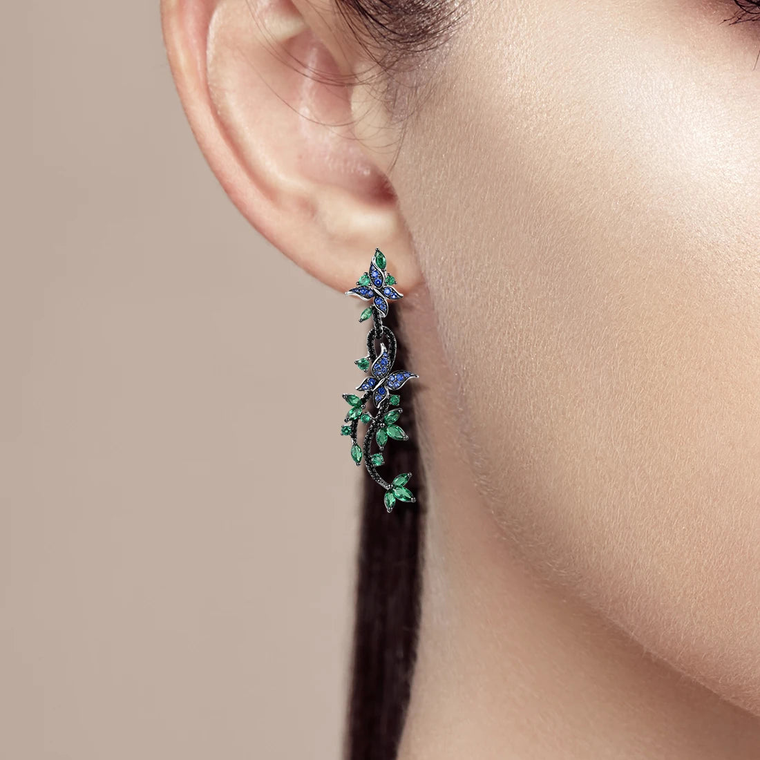 Long silver earrings with blue and green crystal butterflies and vine-like detailing

