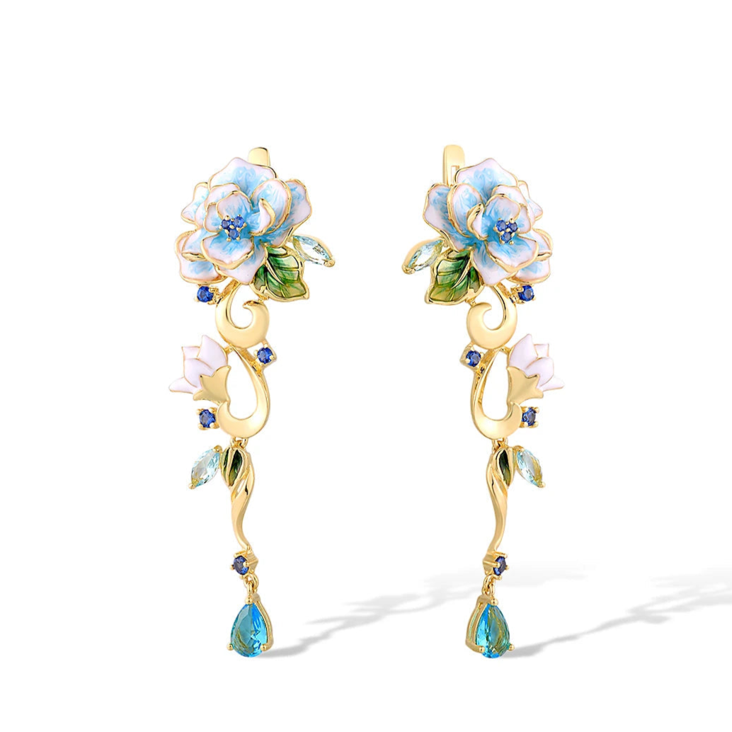 Gold floral earrings with hand-painted white and blue enamel petals, sapphire accents, and dangling blue teardrop stones

