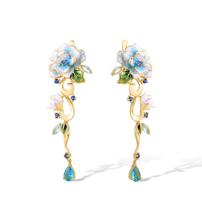 Gold floral earrings with hand-painted white and blue enamel petals, sapphire accents, and dangling blue teardrop stones


