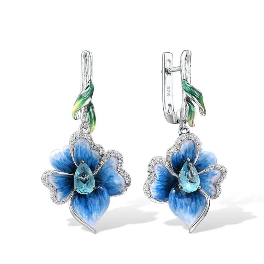 Silver floral earrings with hand-painted blue petals, green enamel accents, and teardrop blue stones.

