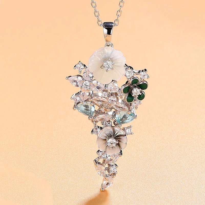 Pendant featuring carved mother-of-pearl flowers, green enamel petals, and aquamarine-blue stones set in silver with white zircon accents.


