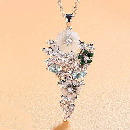 Pendant featuring carved mother-of-pearl flowers, green enamel petals, and aquamarine-blue stones set in silver with white zircon accents.

