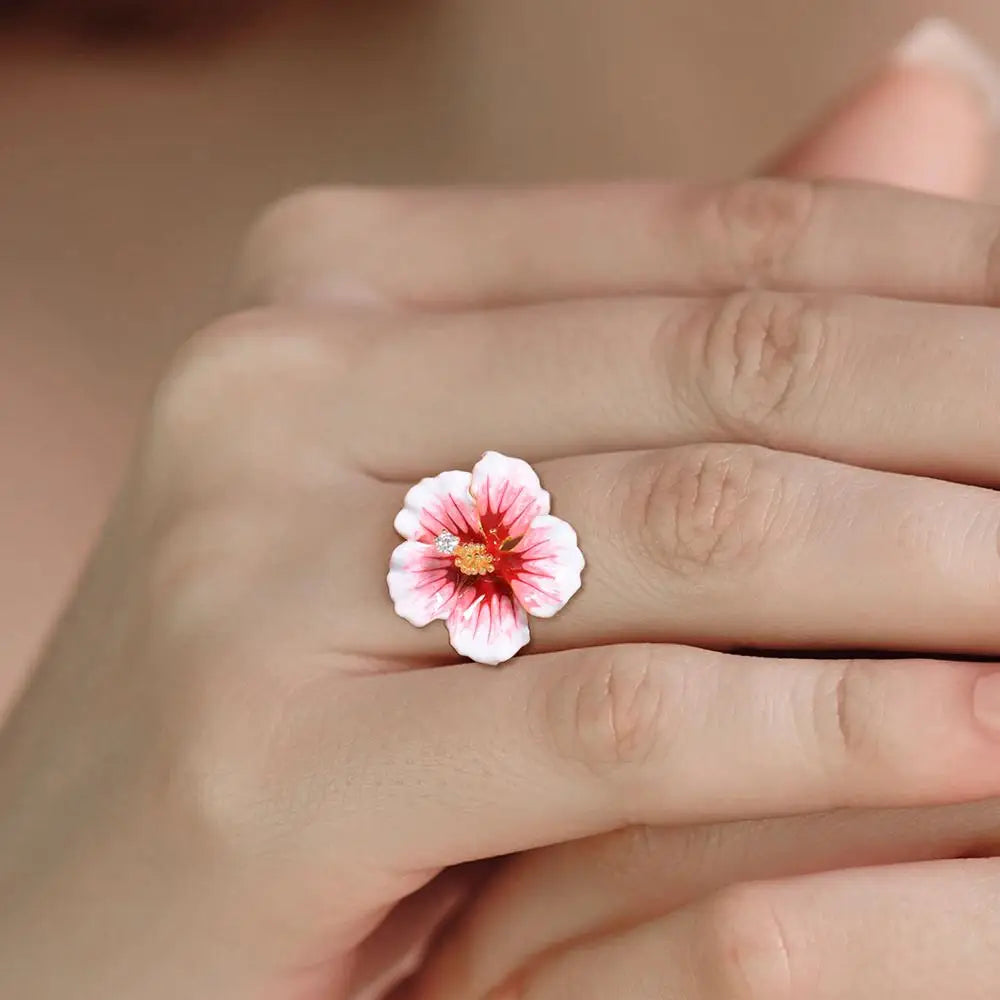 Prato ring shaped like a blooming hibiscus flower in pink enamel with golden stamen and a single sparkling white stone.

