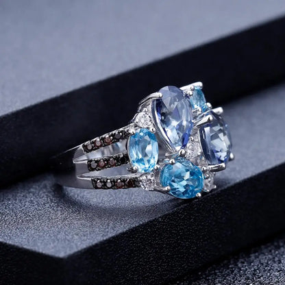 Silver ring featuring an asymmetric cluster of blue and violet gemstones in various cuts

