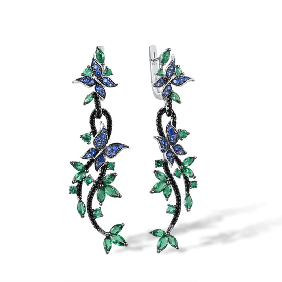 Long silver earrings with blue and green crystal butterflies and vine-like detailing

