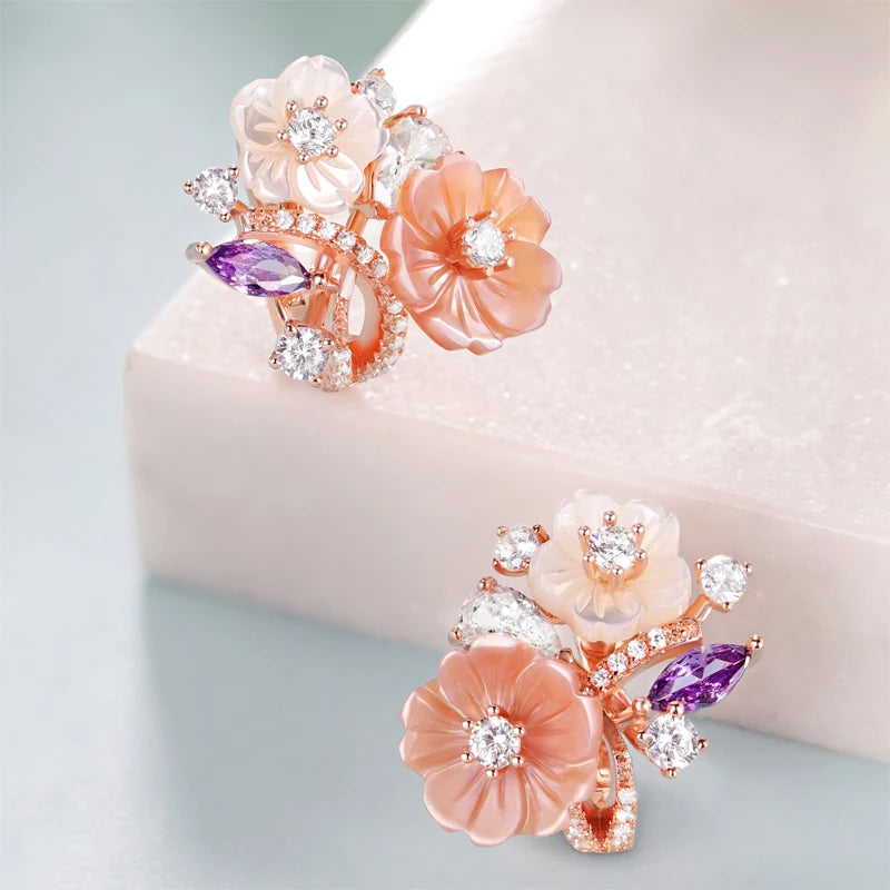 Begonia floral earrings with carved peach and ivory petals, accented by sparkling white and violet stones in a rose gold setting.

