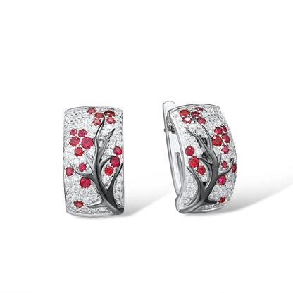 Silver earrings featuring raised black branches with scattered red blossom-like stones.

