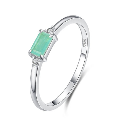 Delicate gold ring with a rectangular light green stone and two small clear side stones.

