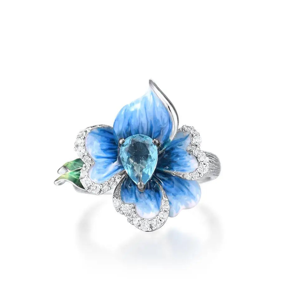 Silver ring with a sculpted blue enamel flower and a central teardrop-shaped blue gemstone surrounded by white stones

