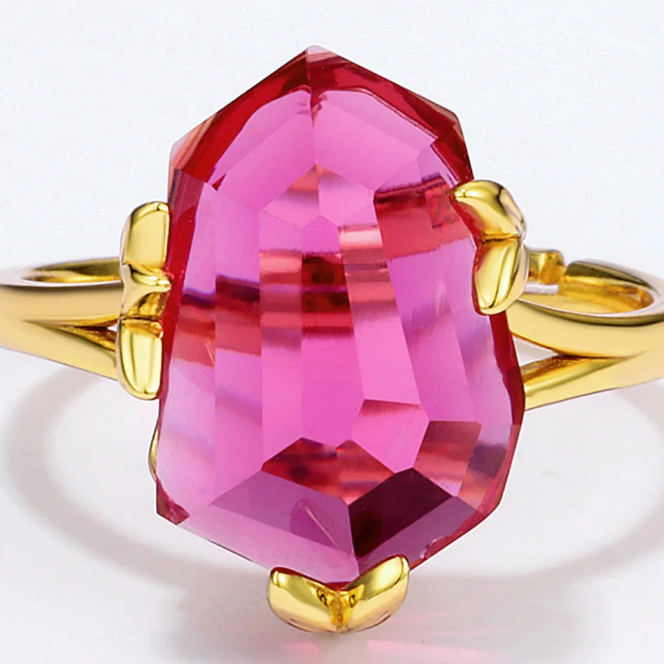 Gold ring with a bold, faceted pink gemstone held by petal-shaped prongs, displayed on a red background.

