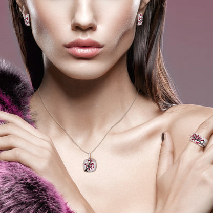 Square silver pendant featuring a black branch with red stones arranged like blossoms.

