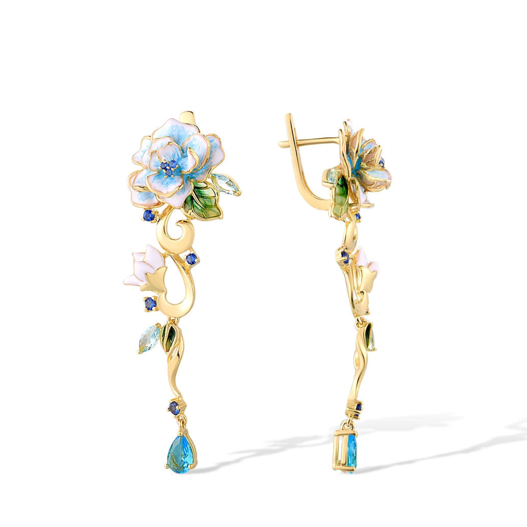 Gold floral earrings with hand-painted white and blue enamel petals, sapphire accents, and dangling blue teardrop stones

