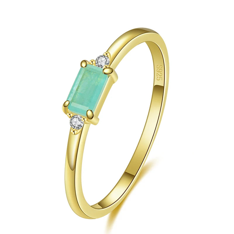 Delicate gold ring with a rectangular light green stone and two small clear side stones.

