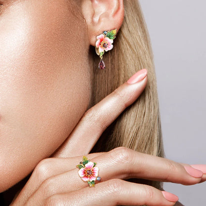 Amaryllis jewelry set with pink enamel flowers, red teardrop stones, green leaf accents, and small blue gemstones on a gold base.

