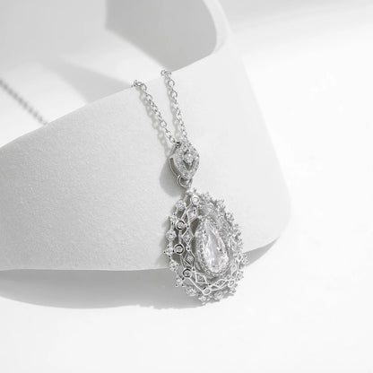 Ornate silver necklace with an intricate teardrop pendant, featuring a central pear-cut white gemstone, part of the Bianco Nero collection.


