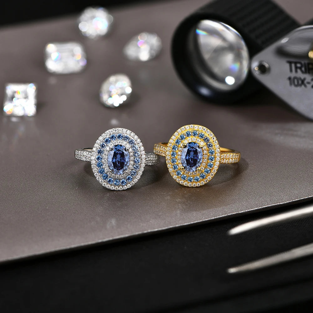 Sterling silver ring with an oval-cut deep blue gemstone surrounded by two concentric halos of white and blue stones, set on a pavé band