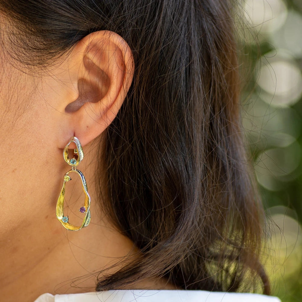 Dangling earrings with flowing gold and silver forms set with turquoise-colored stones

