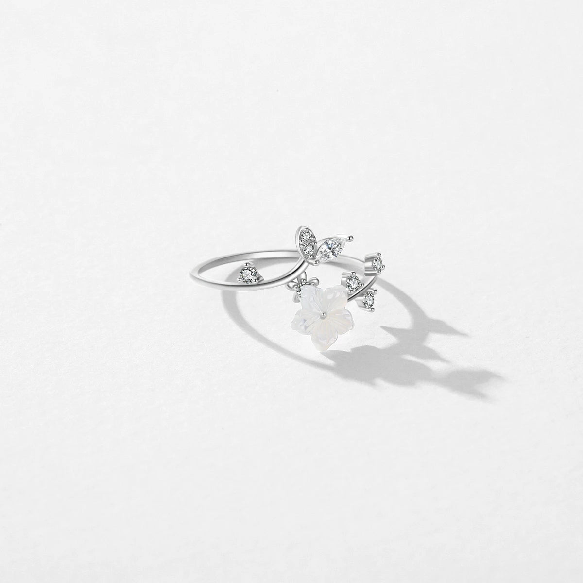 Delicate silver ring featuring a white carved flower and sparkling leaf-shaped stones arranged in a graceful, curved design.

